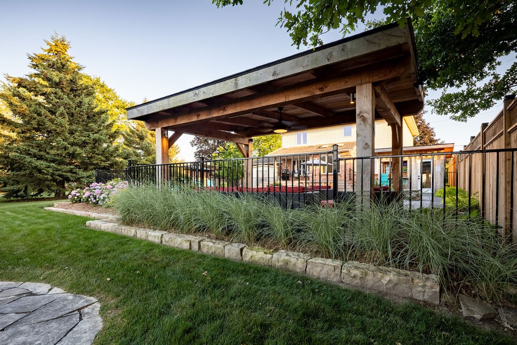 A well-maintained backyard features a wooden gazebo, lush greenery, flowering plants, and a quaint patio area, evoking a serene, inviting atmosphere for relaxation.