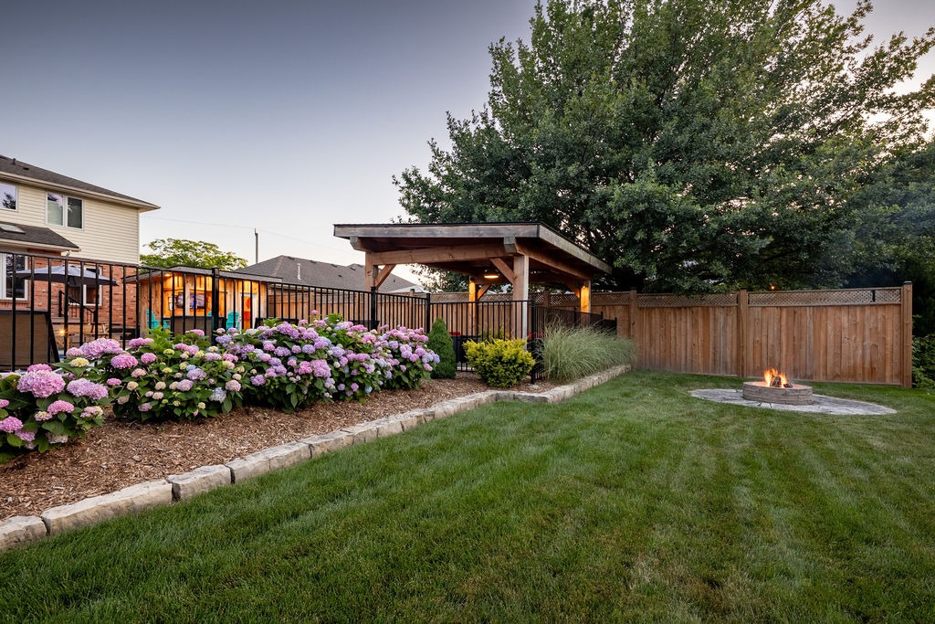 A backyard with vibrant hydrangeas, wooden pergola, and a small fire pit on a neat lawn, enclosed by a wooden fence.