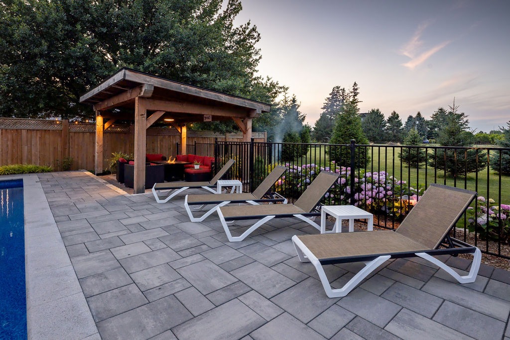 Backyard with swimming pool, lounge chairs, shaded seating area, and surrounding greenery. Relaxing outdoor space with modern design and comfortable atmosphere.