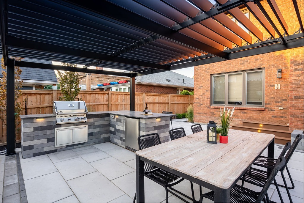 Modern outdoor patio featuring a pergola, dining table, and built-in grill with sleek stone countertops. Simple, stylish backyard setting.