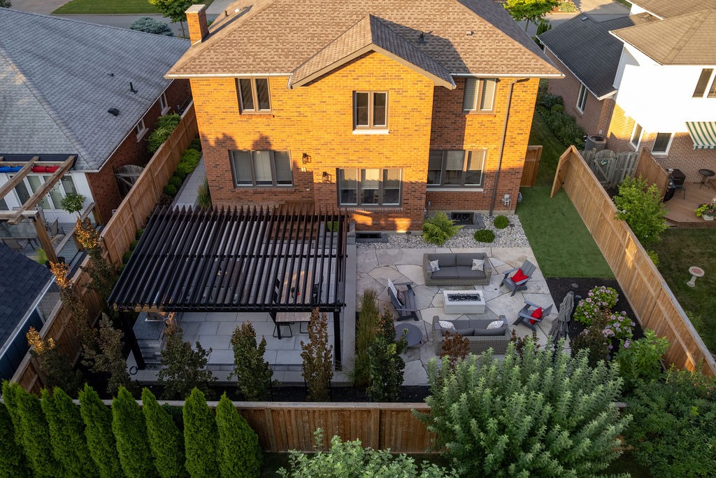 Aerial view of a backyard with brick house, pergola, and patio furniture. Surrounded by a wooden fence and neighboring homes.
