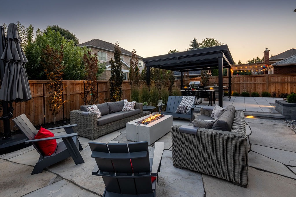 Modern backyard patio with cozy seating, fire pit, and gazebo. Surrounded by wooden fence and greenery, creating a serene outdoor living space.