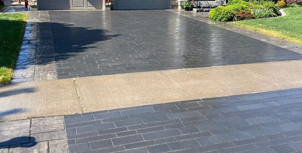 A modern house with two garages, a freshly paved driveway, landscaped yard.