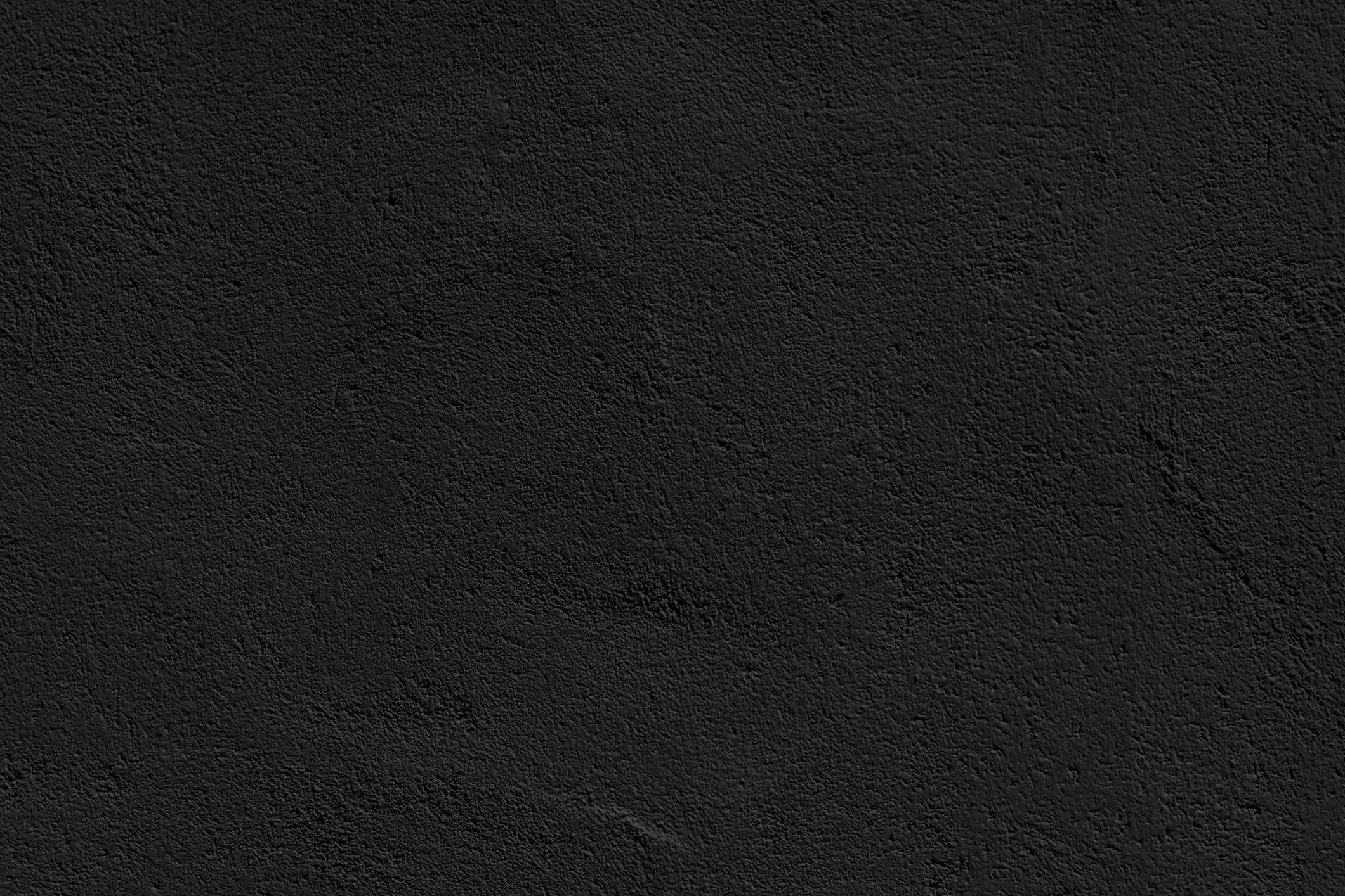 A textured black surface resembling asphalt or concrete, featuring subtle variations in tone and pattern. No landmarks or people present.