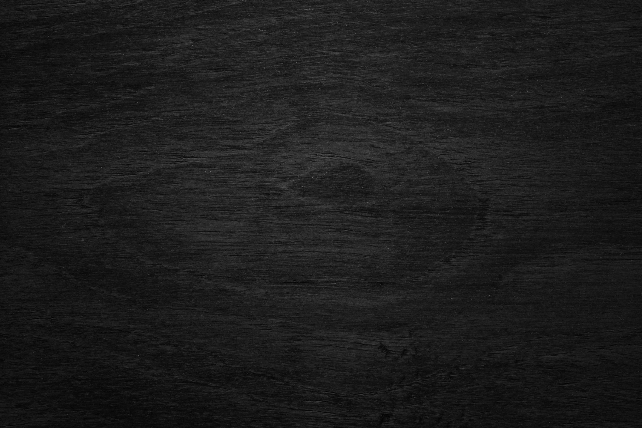 A dark wooden texture with visible grain patterns and a slightly rough surface, showcasing natural wood characteristics and subtle circular markings.